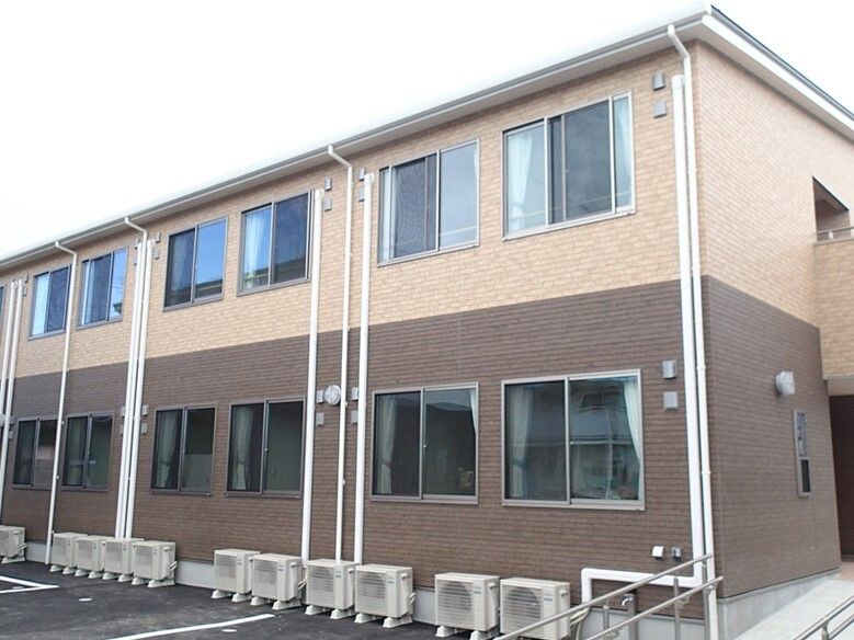 ブラウンとベージュの2色使いの外壁が印象的な2階建ての建物は横に長く、駐車場も付いている。