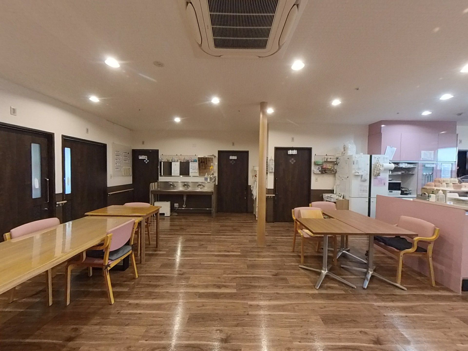 ピンクのエプロンを付けた若い女性スタッフが付き添い、屋外での散歩を楽しんでいる車いすの高齢女性。