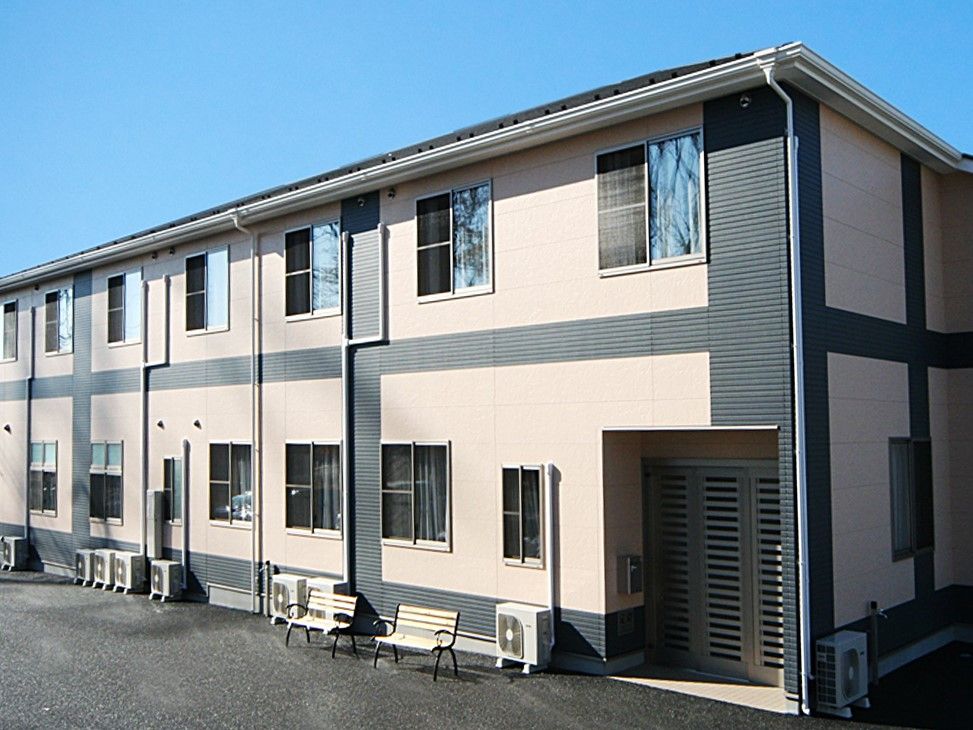 ベージュとグレー、ツートンカラーの外壁で、外にベンチがある2階建て老人ホーム