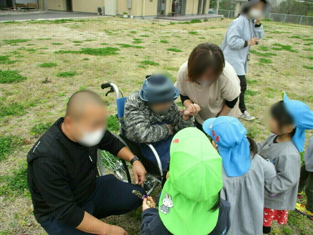 遠くを見ながら笑顔で話している高齢女性と車いすを押す女性スタッフ。散歩の一場面