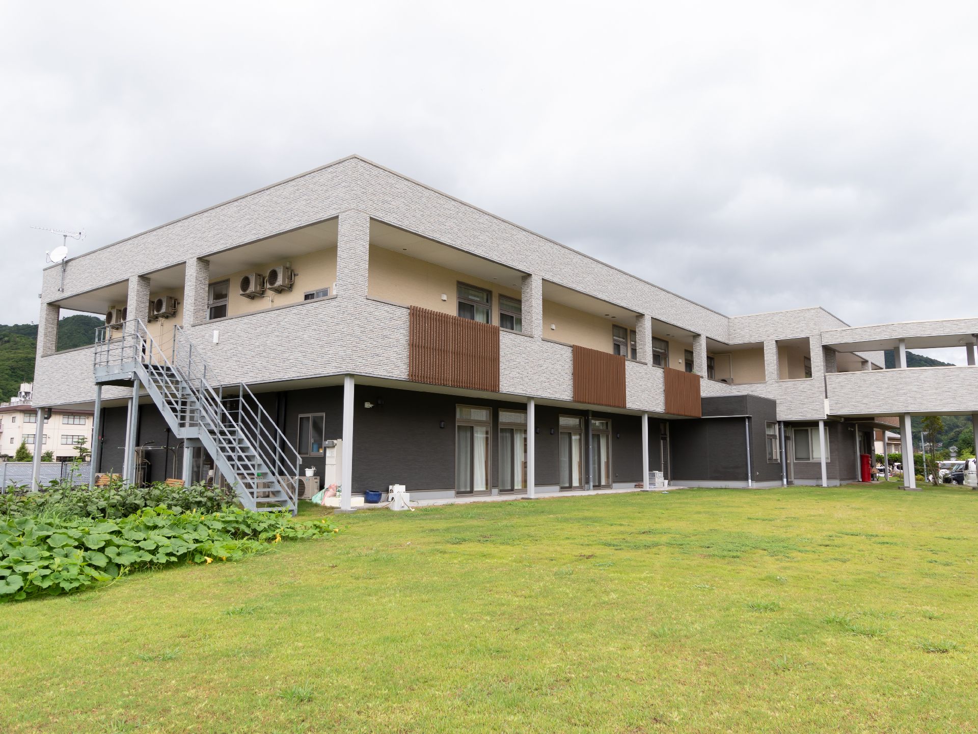 緑に面した２階建ての白い外観の建物