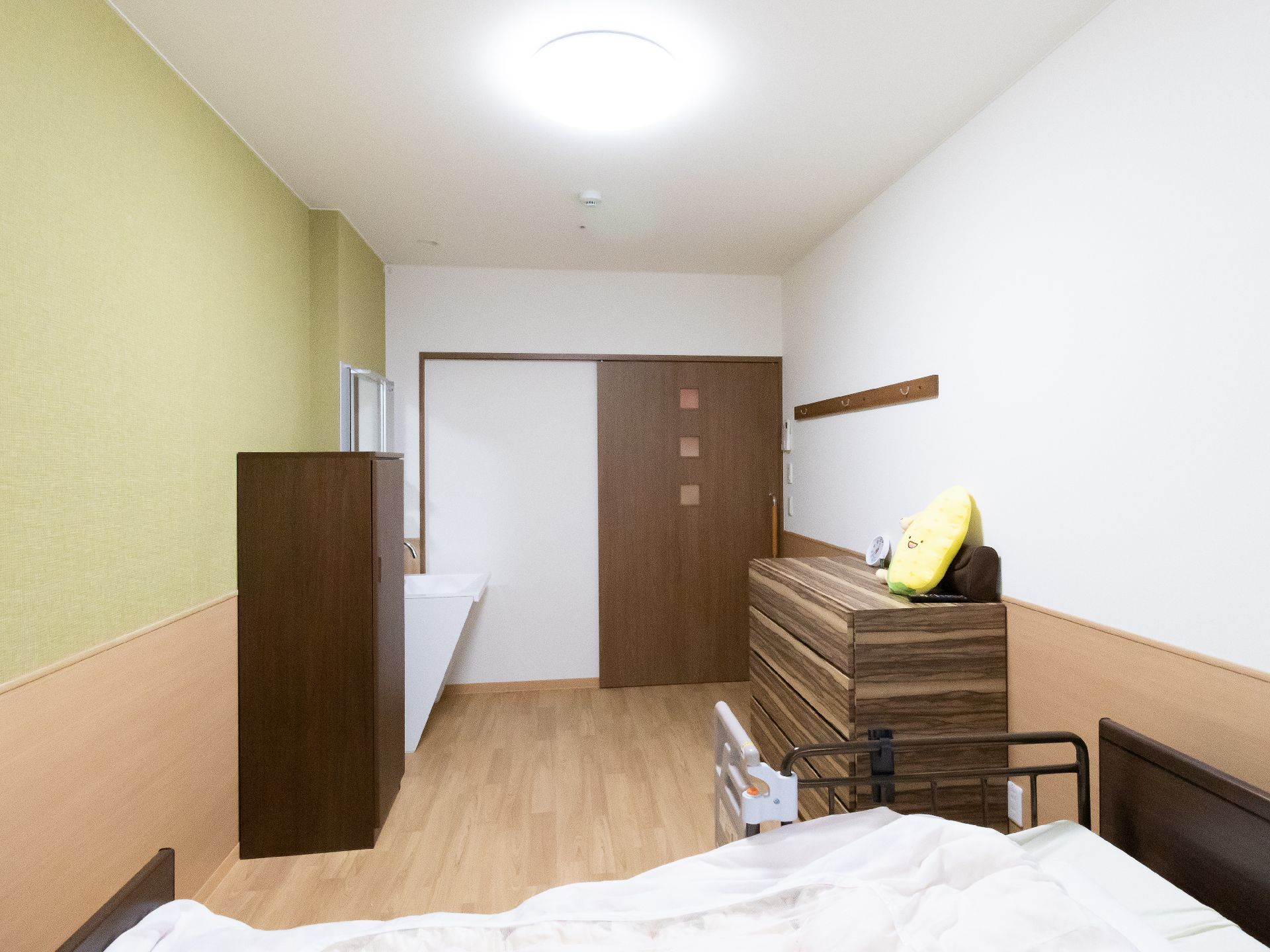 ベッドと木製の棚と白い洗面台が置かれた緑と白の壁の部屋