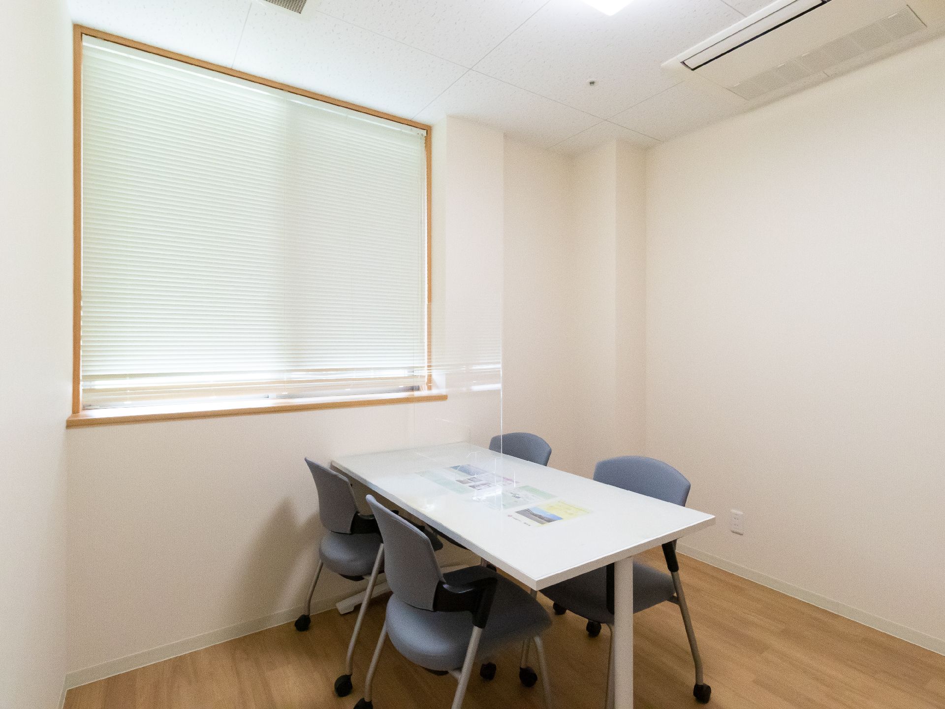 白い壁の部屋の中央に置かれた白い机と４脚の青い椅子