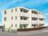 白を基調とした3階建ての建物。各フロアにベランダがあり、１階部分には目隠しとなるフェンスもある。