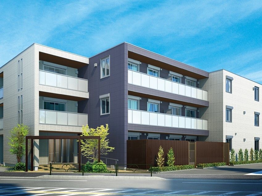 白とダークグレーの3階建ての建物。草木が植えられた敷地内にはフェンスも建てられている。