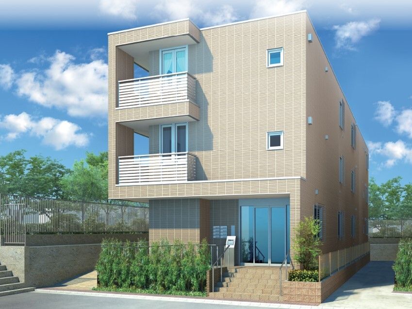 ブラウン系の３階建ての建物の玄関には手すり付きの階段とスロープがあり、草木も植えられている。