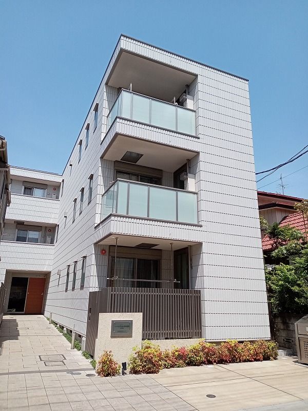 エル字型の白を基調とした3階建ての建物。ブラウンのフェンスに囲まれ、敷地内には駐車場がある。
