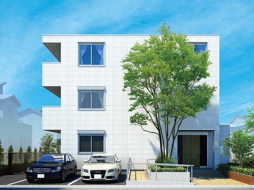 白を基調とした3階建ての建物の玄関には手すり付きのスロープがあり、木も植えられている。
