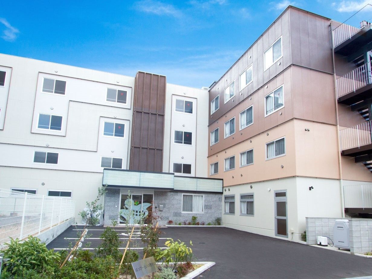 4階建ての建物がある敷地内には駐車場もあり、エル字型で白とブラウン系でまとめられている。