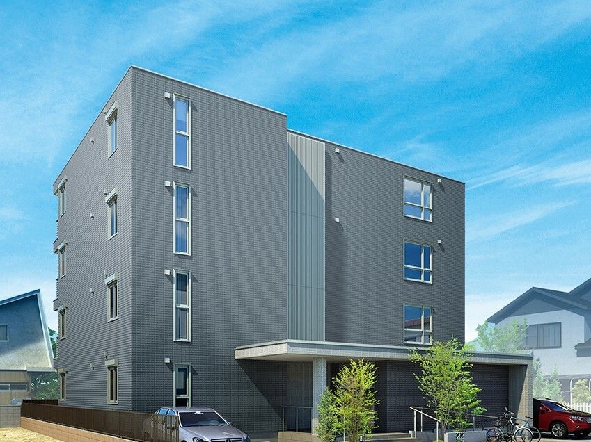 ４階建ての建物はグレー系の外観で、建物の前には駐車場と駐輪場があり、玄関には屋根が付いている。