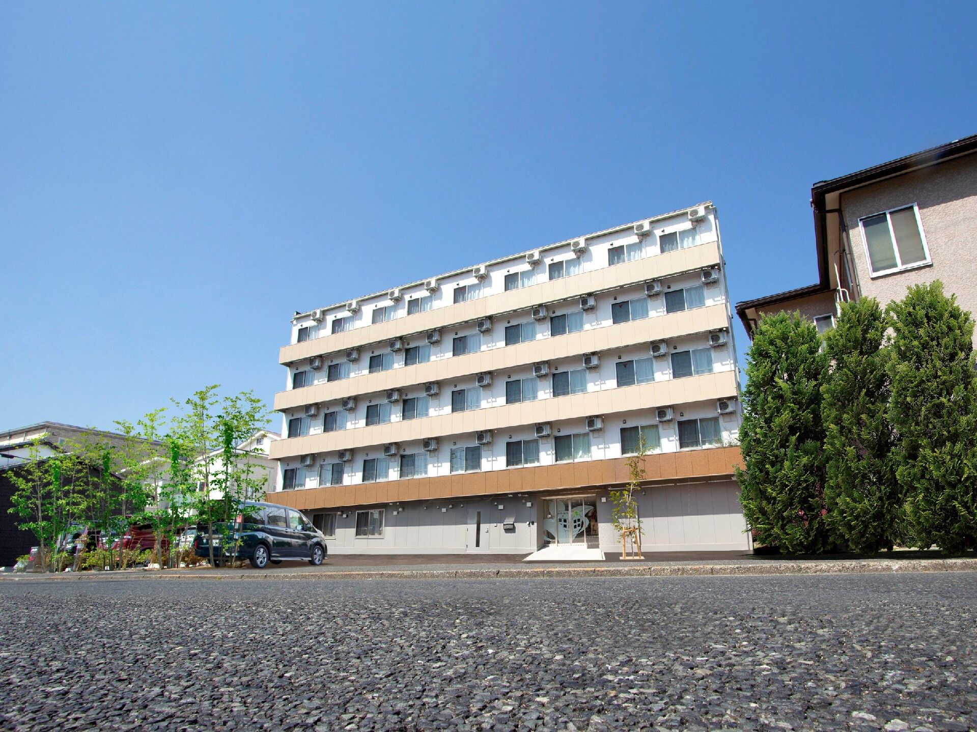 道路に面した場所に建っている5階建ての建物にはベランダが付き、敷地内には駐車スペースもある。