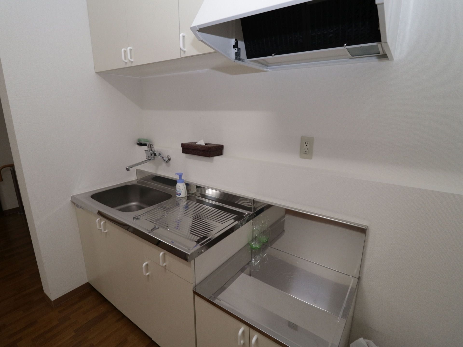 居室には、白を基調としたキッチンが完備されている。壁に棚が備わっており、テッシュやスポンジが置かれている。
