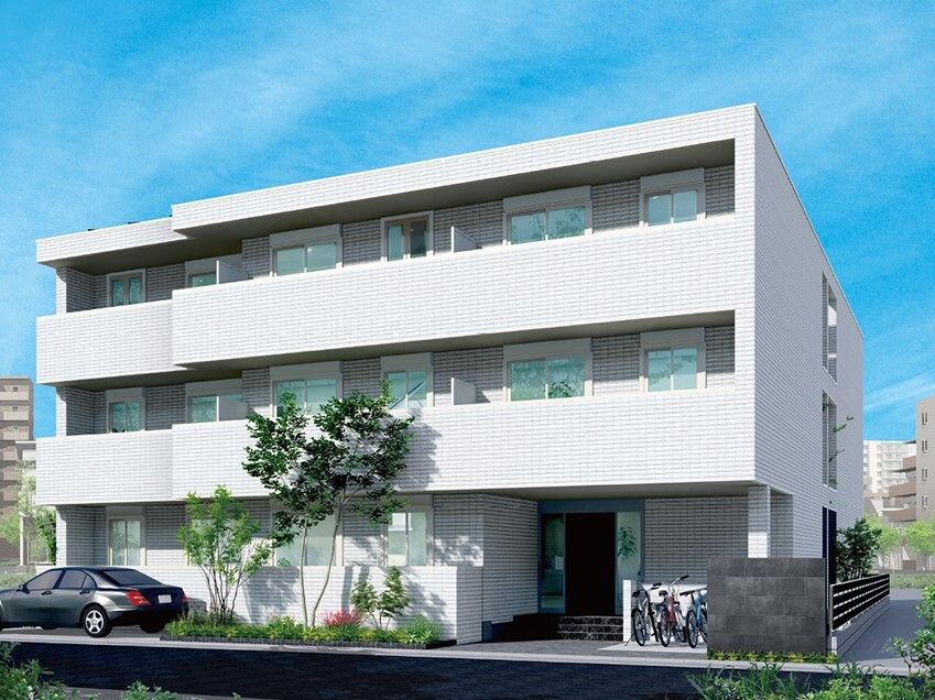 白を基調とした3階建ての建物。建物の前には駐車場があり、駐輪場もある。草木も植えられている。