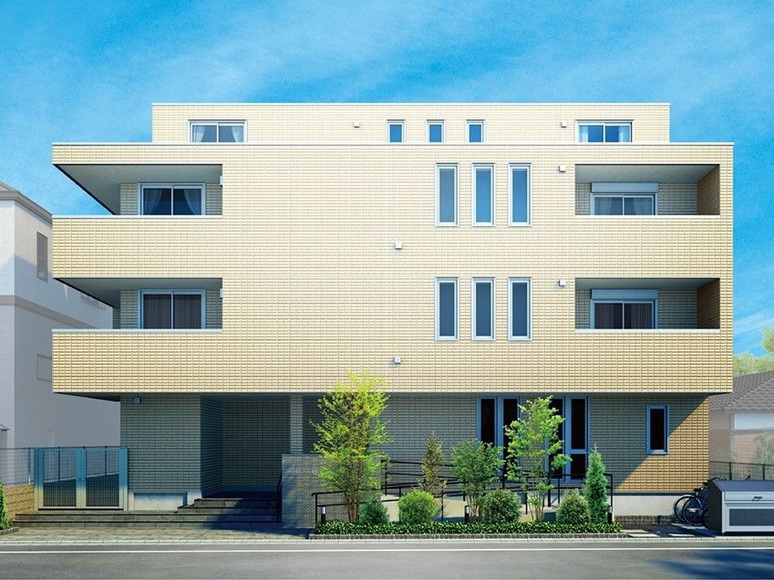 4階建ての建物は日当たりのいい場所に建っている。ベージュ系の外壁で玄関先には手すり付きのスロープと階段もある。