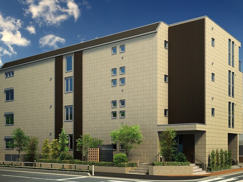 玄関に手すり付きの階段が設置されたベージュ系の４階建ての建物の周りには草木が植えられている。