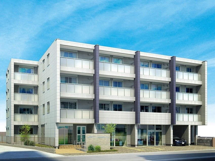 4階建ての建物は白を基調としていて、後ろにも同じデザインの建物がある。建物前には駐車場もある。