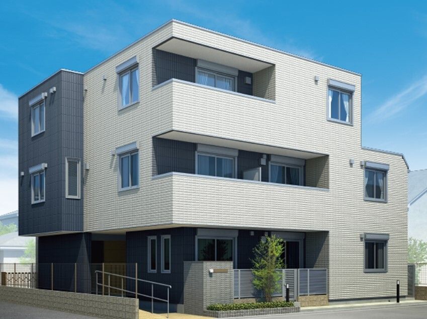 グレーの外壁の3階建ての建物は各フロアにベランダがあり、玄関先には手すり付きのスロープがあり、門のそばには木も植えられている。