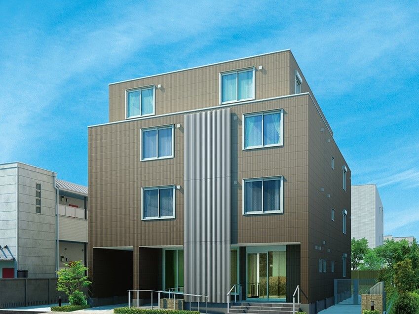 ブラウン系の建物は3階建てで周りには草木が植えられ、玄関先には手すり付きのスロープと階段が設置されている。