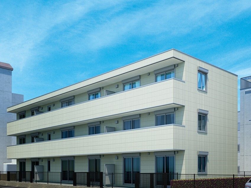 白を基調とした3階建ての建物は各フロアにベランダがあり、シンプルなデザイン。周囲にも建物がある。