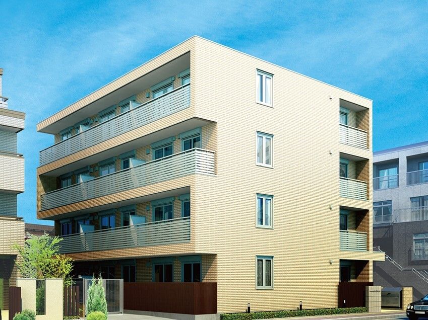 ４階建ての建物はベージュを基調とした落ち着いた色合いで、各フロアにベランダがある。周りにも同じ高さくらいの建物がある。