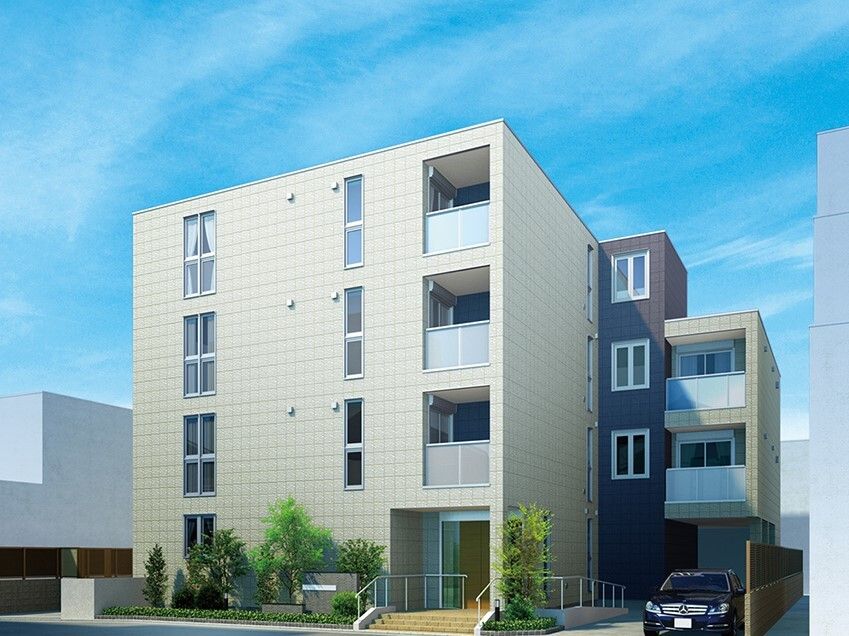 4階建ての建物は白とダークブラウンで草木が周りに植えられ、玄関には手すり付きのスロープと階段があり、門には住宅名が書かれている。