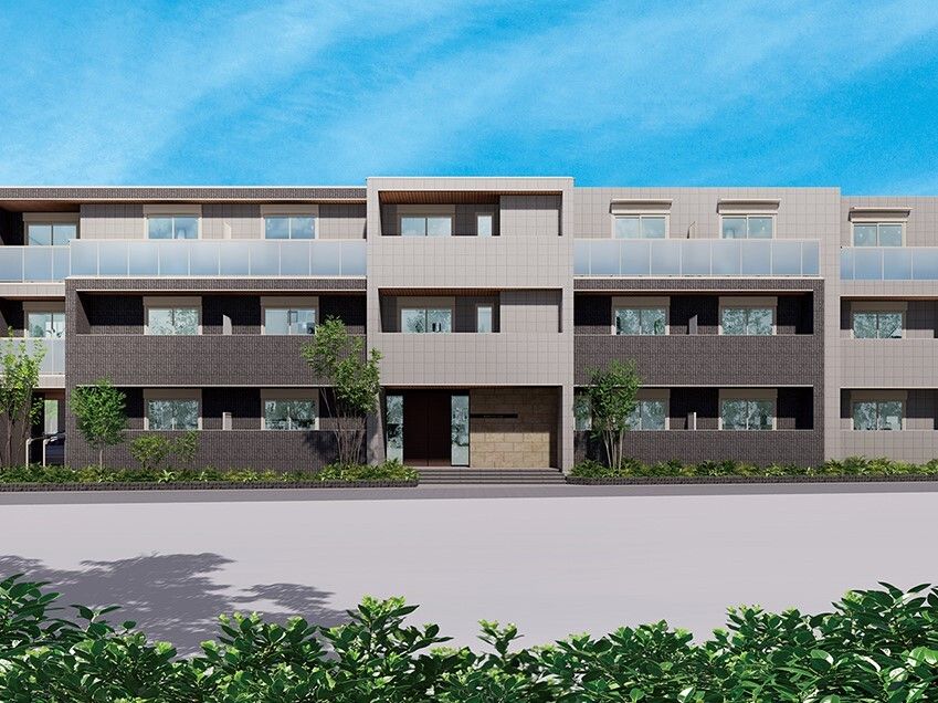 ブラウン系の3階建ての建物は横に長く、目の前に広い空き地があり、周りには草木が植えられている。