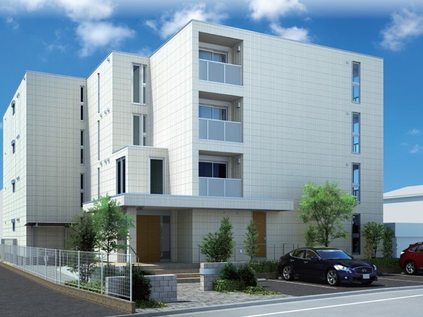 白を基調とした４階建ての建物。周りには草木が植えられ、駐車スペースには車が止められ、玄関には屋根も付いている。