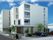4階建ての建物は日当たりのいい場所に建っている。白を基調としていて、建物のそばの駐車スペースには車も止まっている。