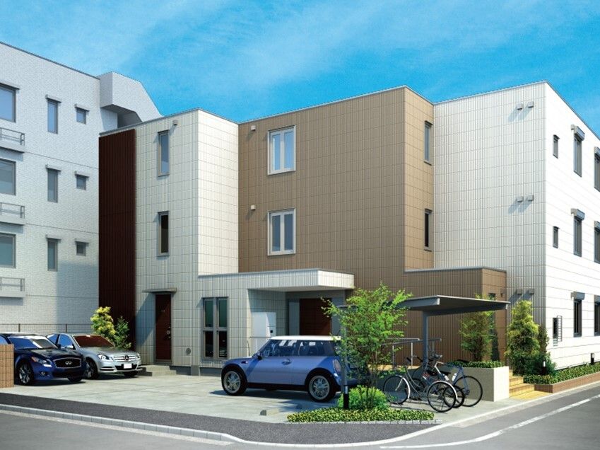 白とブラウンの建物の玄関には屋根が付き、敷地内には駐車場と駐輪場もあり、車や自転車が止められている。