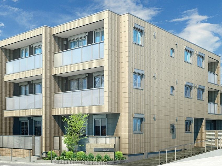 日当たりのいい場所に建っている3階建ての建物の玄関に手すり付きのスロープがあり、草木が植えられている。