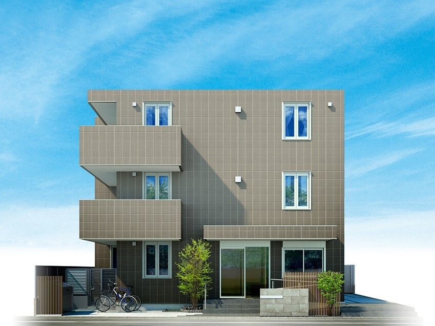 ブラウン系の建物は3階建てで窓が多く、玄関前には自転車が止められている。目隠しともなるフェンスもある。
