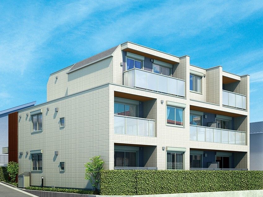 草木が植えられている敷地にある3階建ての建物は白を基調としていて、各フロアにベランダが付いている。
