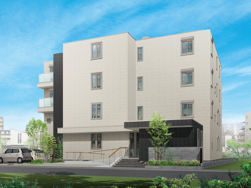 白を基調とした４階建ての建物。玄関には屋根があり、手すり付きのスロープと階段が設置されている。