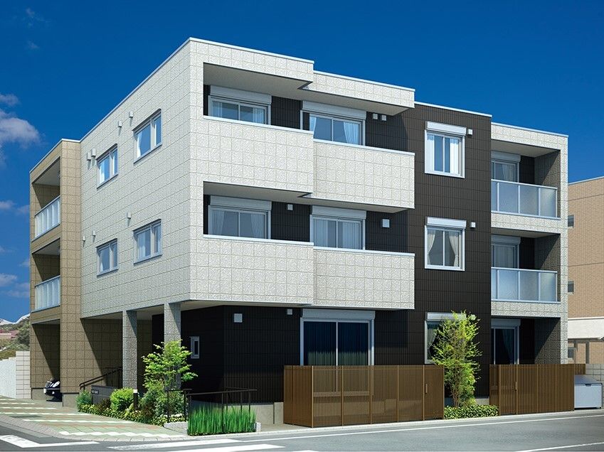 白を基調とした3階建ての建物。黒とブラウンのアクセントがあり落ち着いた雰囲気。草木も植えられ、1階部分は駐車場にもなっている。