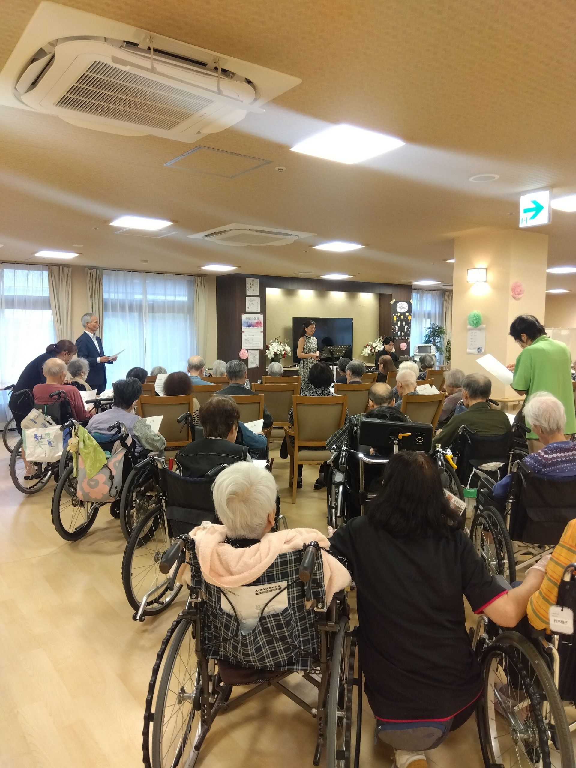 高齢者2名とスタッフが手を握りながら談笑している様子。施設内の会話の一画面