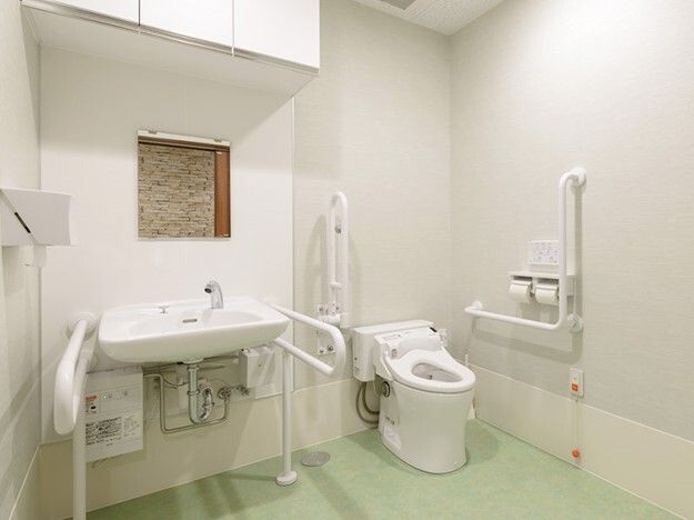 手すりが両サイドに設置されたトイレと手洗い場。オレンジの呼び出しボタンも下の方についている。