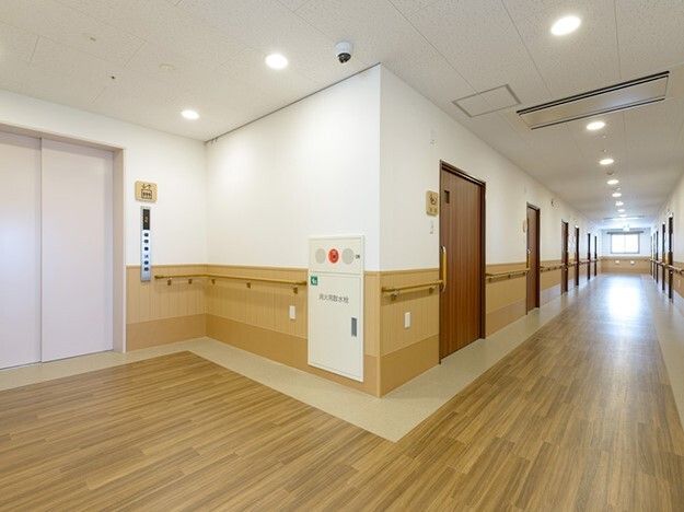 まっすぐな廊下には手すりが付き、突き当りには大きな窓がある。左側にはエレベーターが付いている。