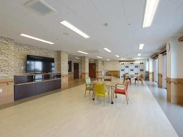 大きなテレビが設置された食堂にはカラフルな椅子がセットされたテーブルが置かれ、左側には廊下もある。