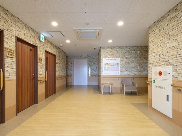 併設事業所の名前が書かれたドアが室内にあり、すぐそばにはトイレがあり、幅の広い廊下にはいすも置かれている。