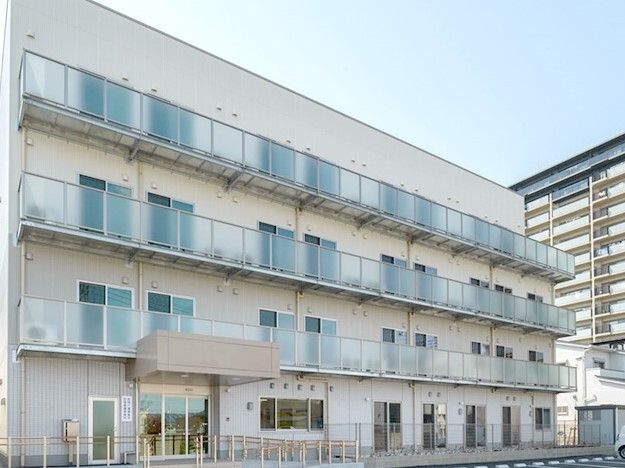 4階建ての建物の各フロアにベランダがあり、白を基調としたさわやかな外観。玄関には屋根がある。