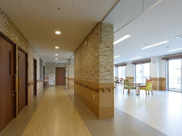 居室のドアが左側に並んで設置され、廊下には手すりが付き、右側にはダイニングテーブルが置かれた食堂がある。