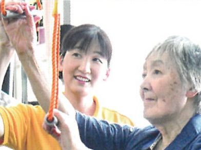 こちらを向いて笑顔になる車いすの高齢女性と介護施設の女性スタッフの様子