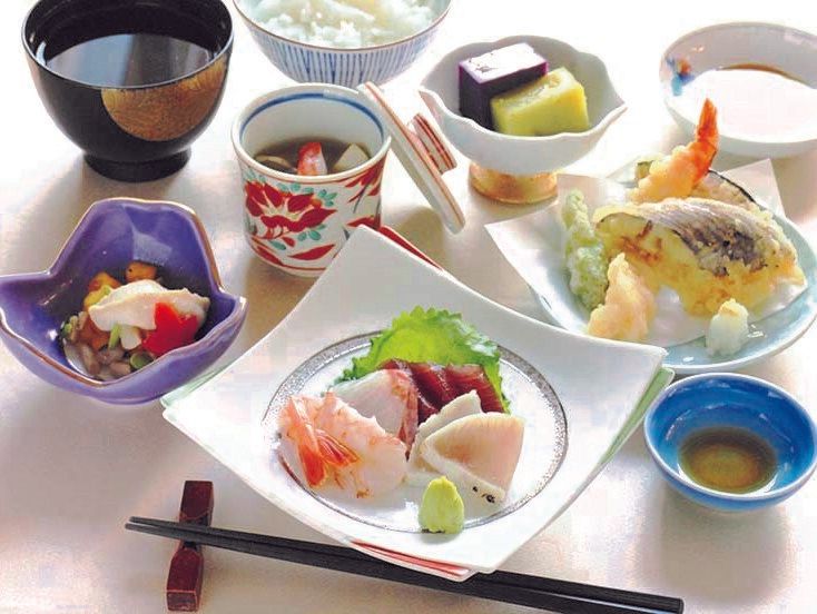 白いご飯に汁物、天ぷらの盛り合わせ、刺身や野菜の小鉢などがきれいな器に盛られて並んでいる。