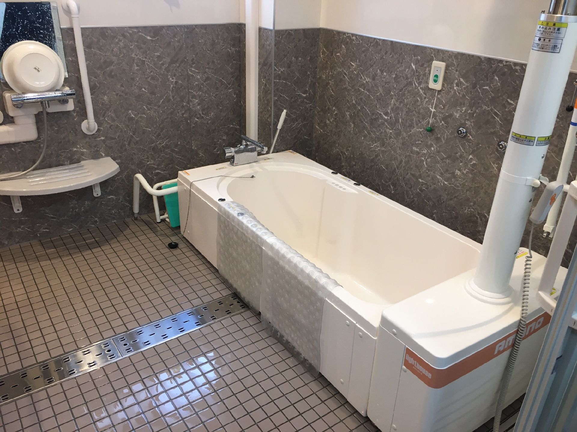 ブルーのユニフォームを着た男性スタッフと高齢女性が並んで座り、ロープを使った機能訓練を行っている。