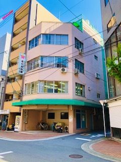 白いゆったりとした服を着た高齢女性がそばにいる車いすの高齢男性の肩に手を置き、笑顔で話かけている。
