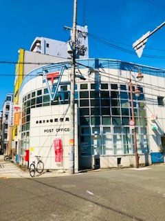 郵便局の名前が書かれた外壁にはPOST OFFICEと英文字でも書かれている。自転車が止められ、その後ろに大きな建物がある。