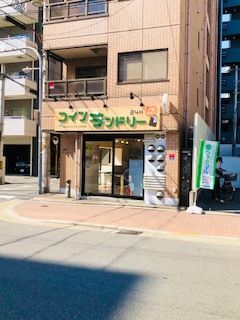 グリーンの文字でコインランドリーと書かれたベージュ系の建物。建物の前にはのぼりも立っている。