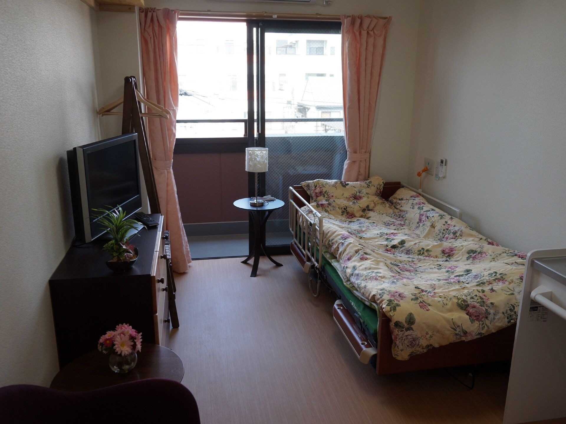 寝具付きのベッドやテレビ、タンスなどが置かれた部屋には大きな窓があり、ベランダも設置されている。