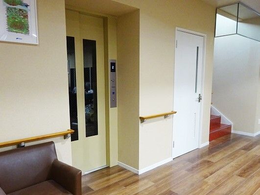手すりが設置された館内にはエレベーターもあり、エレベーターのすぐそばにはブラウンのソファもある。