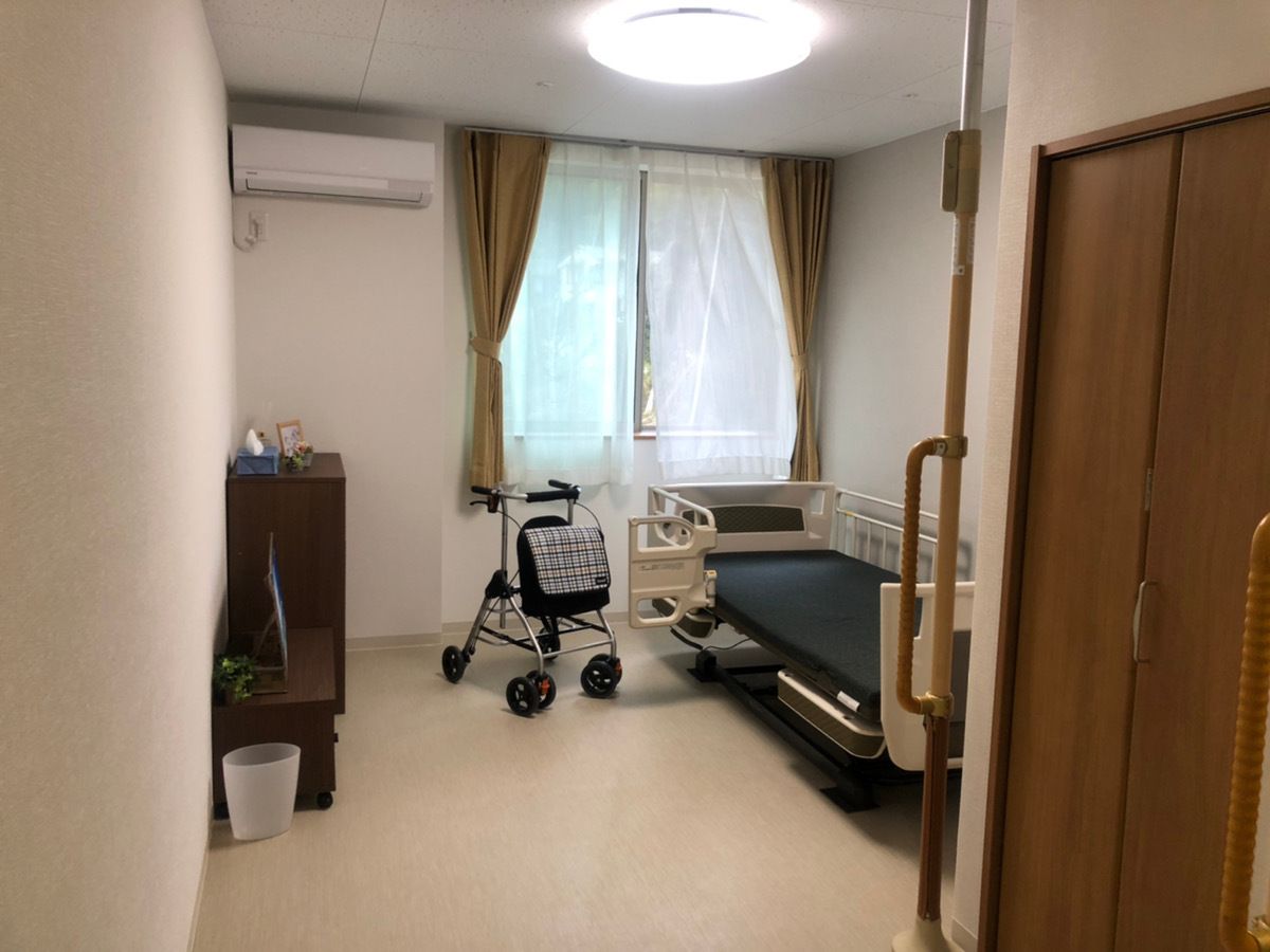 車いすに乗る女性と笑顔でそれを押すスタッフ。二人で散歩しながら会話している様子
